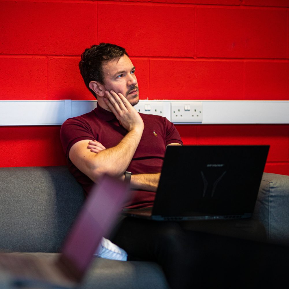 Danny presenting some important information sat on a sofa with his large laptop